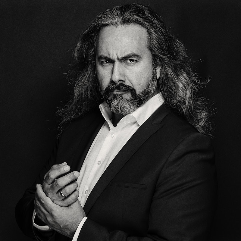 Intensives Schwarz-Weiß-Schauspielerportrait eines Mannes mit langen Haaren und Bart im Anzug, aufgenommen für eine professionelle Sedcard in Freising.